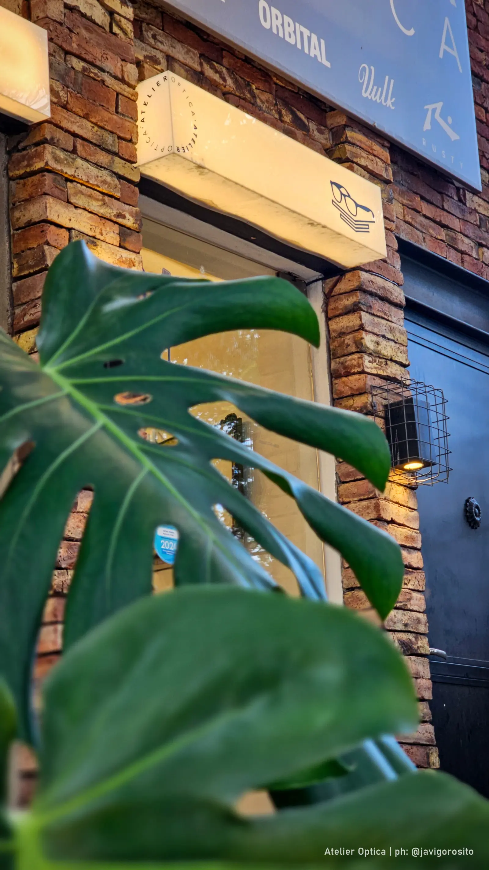 Fachada de ladrillo de Atelier Óptica en Córdoba con farol y plantas